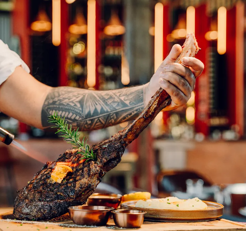 A 1.5kg tomahawk steak held up on the bone, off the grill